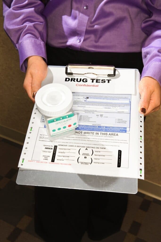 Collector holding a confidential drug test form and specimen cup for on-site hiring event testing